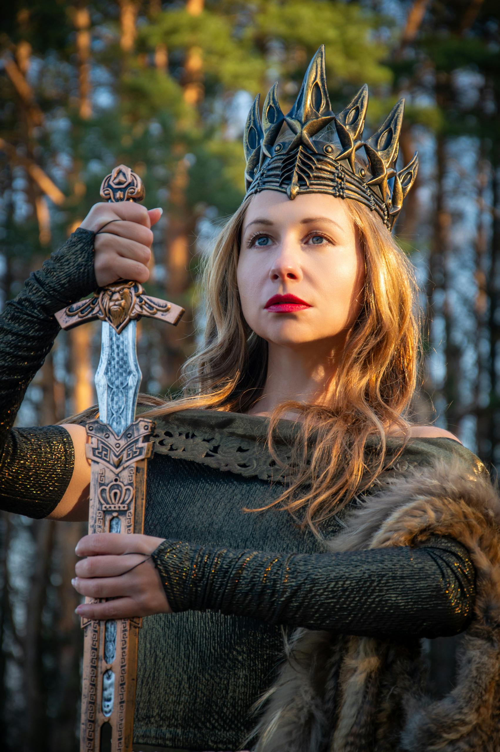 A regal woman in armor holding a sword amidst a forest backdrop.